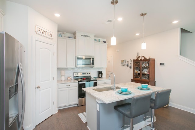 kitchen featuring an island with sink, appliances with stainless steel finishes, white cabinets, and decorative light fixtures