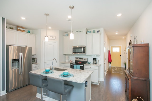 kitchen with sink, decorative light fixtures, stainless steel appliances, a kitchen island with sink, and white cabinets