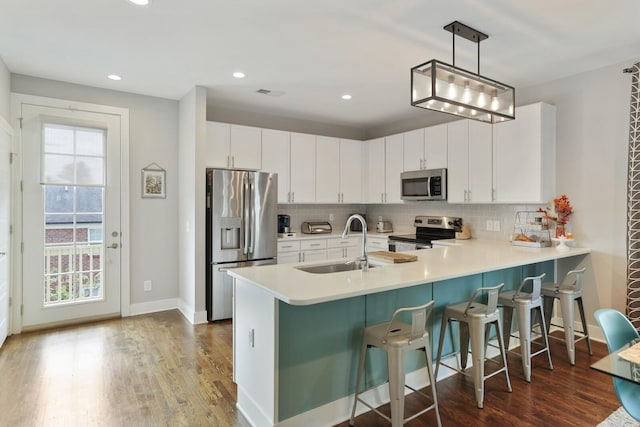 kitchen with sink, white cabinetry, hanging light fixtures, stainless steel appliances, and tasteful backsplash