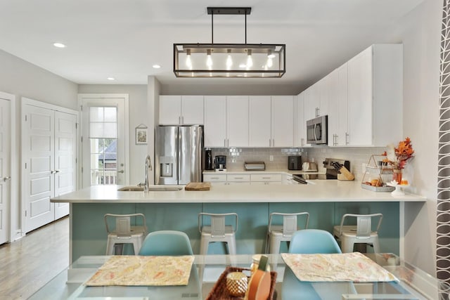 kitchen with white cabinetry, a breakfast bar area, hanging light fixtures, kitchen peninsula, and stainless steel appliances