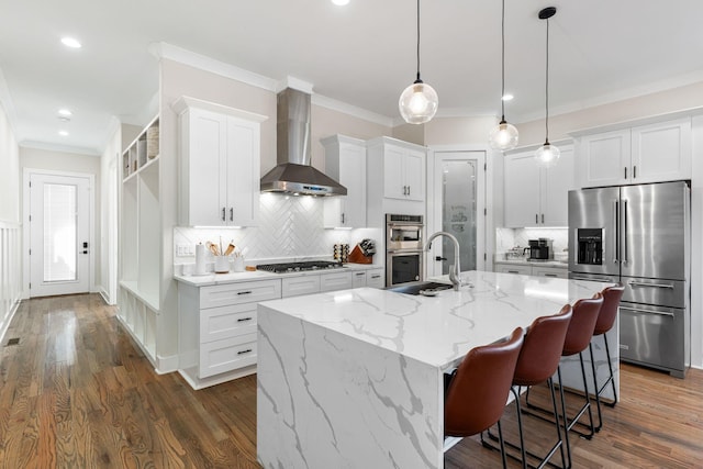 kitchen featuring crown molding, stainless steel appliances, white cabinetry, a sink, and wall chimney range hood