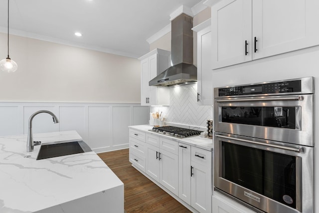 kitchen with tasteful backsplash, wall chimney exhaust hood, appliances with stainless steel finishes, ornamental molding, and a sink