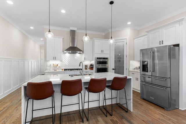 kitchen featuring stainless steel appliances, white cabinetry, a sink, wall chimney range hood, and wood finished floors