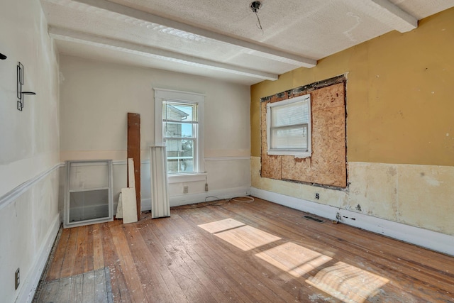 unfurnished room featuring hardwood / wood-style floors, a textured ceiling, and beam ceiling