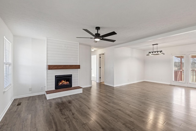 unfurnished living room with ceiling fan, a large fireplace, a textured ceiling, and dark hardwood / wood-style floors