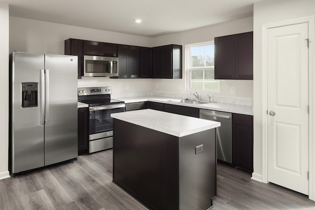 kitchen with sink, dark brown cabinets, light wood-type flooring, appliances with stainless steel finishes, and a kitchen island