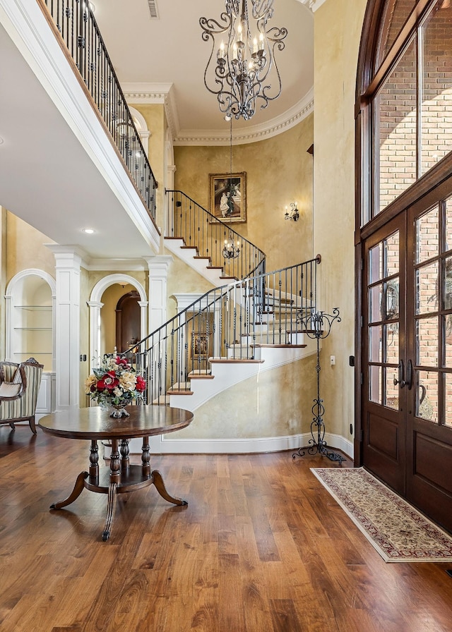 entryway with a high ceiling, wood-type flooring, ornamental molding, french doors, and ornate columns