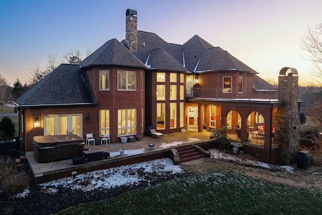 back house at dusk featuring a hot tub, a patio, a balcony, and central AC unit