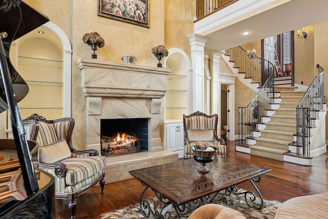 living room featuring built in shelves, ornate columns, dark hardwood / wood-style flooring, a high end fireplace, and a high ceiling