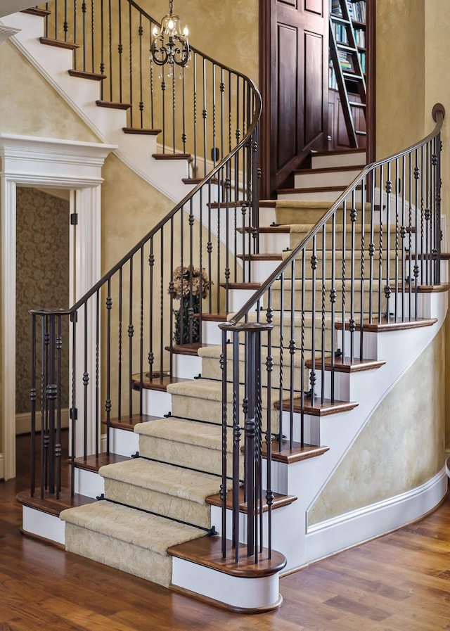 staircase with a high ceiling, hardwood / wood-style floors, and a notable chandelier