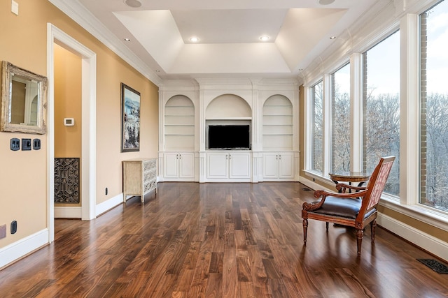 living room featuring built in shelves, ornamental molding, a tray ceiling, and dark wood-type flooring