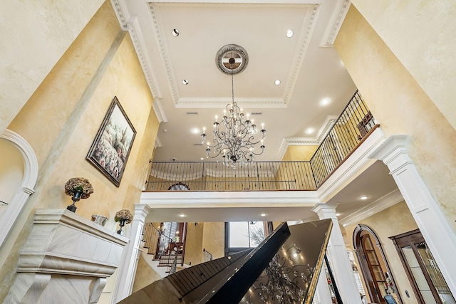 stairs featuring ornate columns, crown molding, a towering ceiling, and a notable chandelier