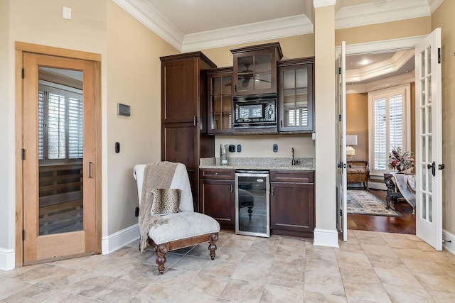 bar with dark brown cabinetry, sink, light stone counters, black microwave, and beverage cooler