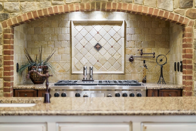 kitchen featuring stainless steel gas stovetop, light stone countertops, and decorative backsplash