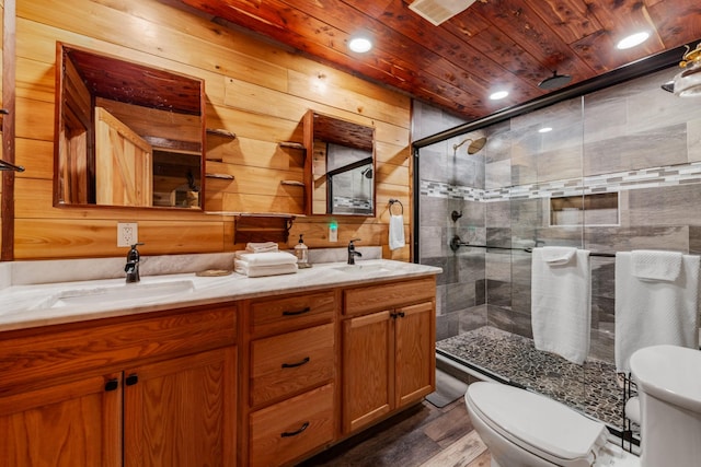 bathroom with toilet, a shower with shower door, wooden ceiling, vanity, and wooden walls