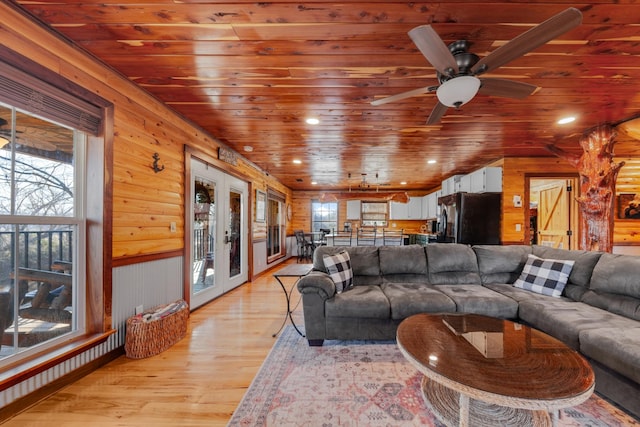 living room with wood walls, ceiling fan, wooden ceiling, light wood-type flooring, and french doors