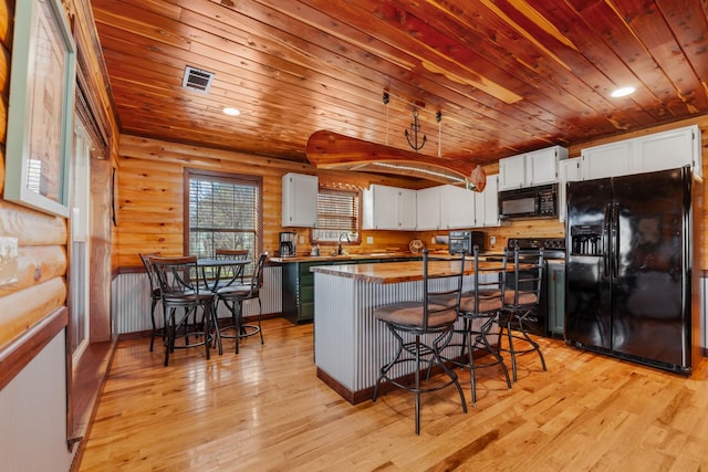 kitchen featuring white cabinetry, a center island, black appliances, a kitchen bar, and log walls