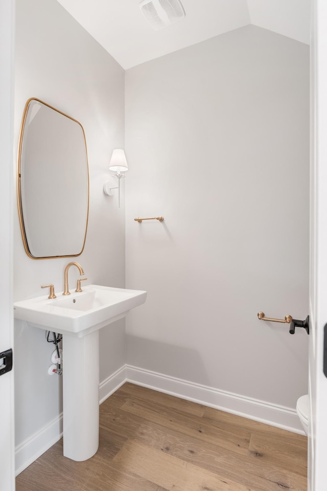 bathroom featuring wood-type flooring, toilet, and vaulted ceiling