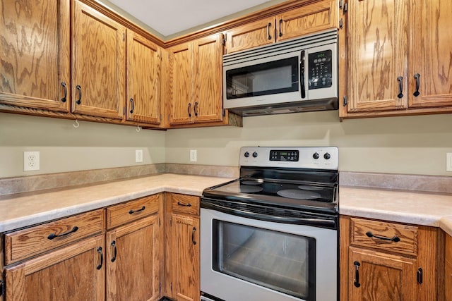 kitchen with stainless steel appliances, brown cabinetry, and light countertops