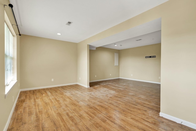 empty room with light wood finished floors, visible vents, and baseboards