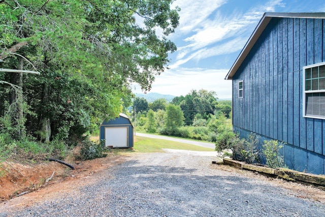 view of side of home with an outbuilding, a storage shed, gravel driveway, and a garage