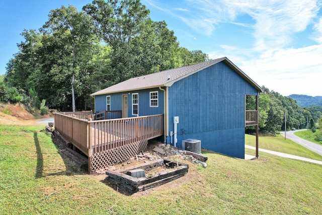 rear view of house with a shingled roof, a vegetable garden, a lawn, a wooden deck, and central AC