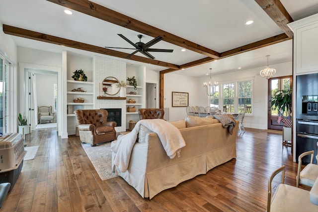 living room featuring beamed ceiling, dark wood-type flooring, ceiling fan with notable chandelier, and a fireplace