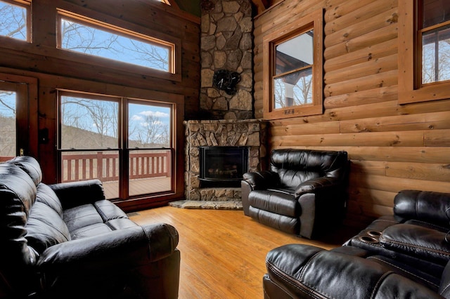 living room featuring a stone fireplace, wood-type flooring, rustic walls, and a towering ceiling