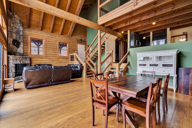 dining room with a stone fireplace, beam ceiling, high vaulted ceiling, log walls, and light wood-type flooring