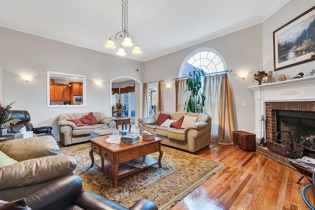 living room featuring crown molding, light wood-type flooring, a chandelier, and a fireplace