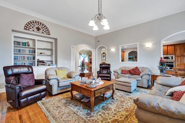 living room featuring ornamental molding, light hardwood / wood-style flooring, an inviting chandelier, and built in shelves