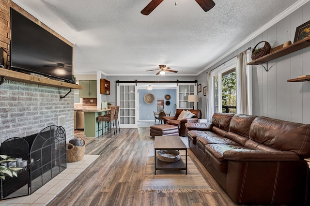 living room featuring hardwood / wood-style floors, a fireplace, ceiling fan, crown molding, and a barn door