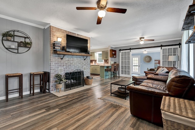 living room with a barn door, wood-type flooring, a textured ceiling, ornamental molding, and a fireplace