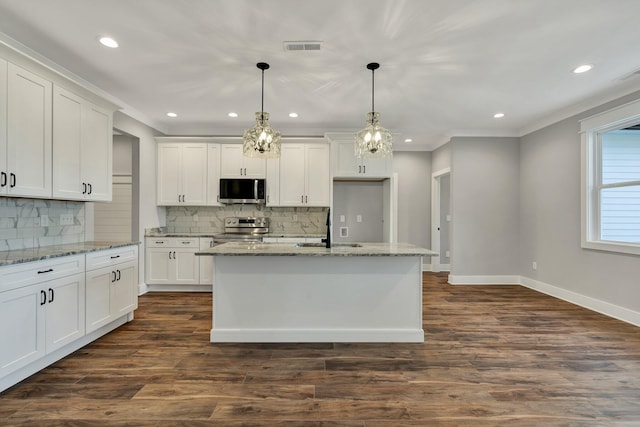 kitchen featuring appliances with stainless steel finishes, decorative light fixtures, white cabinets, light stone countertops, and a center island with sink