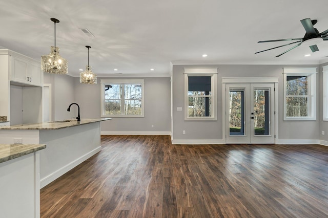 kitchen with white cabinetry, dark hardwood / wood-style flooring, hanging light fixtures, ornamental molding, and light stone counters