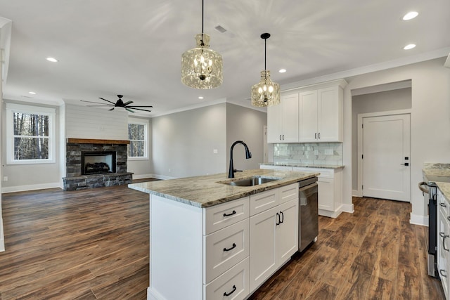 kitchen featuring a fireplace, decorative light fixtures, sink, white cabinets, and a center island with sink