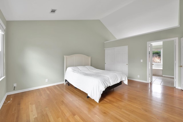 bedroom with vaulted ceiling, a closet, ensuite bathroom, and light hardwood / wood-style flooring