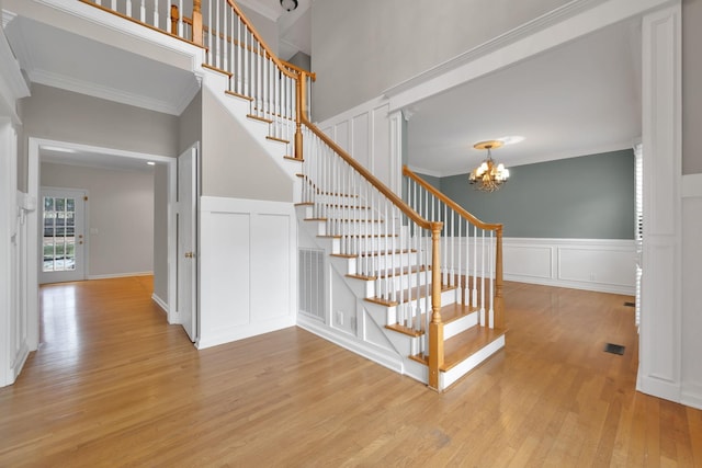 staircase with a towering ceiling, wood-type flooring, ornamental molding, and a chandelier