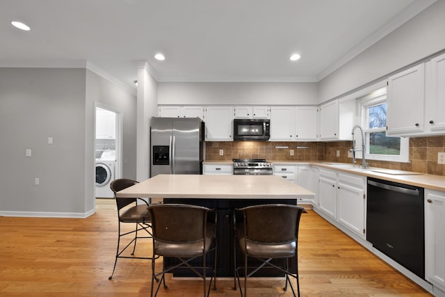 kitchen with washer / dryer, a kitchen breakfast bar, a center island, and appliances with stainless steel finishes