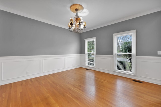 empty room featuring an inviting chandelier, ornamental molding, and light hardwood / wood-style floors