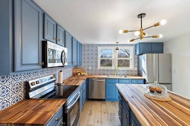 kitchen featuring wood counters, blue cabinets, sink, pendant lighting, and stainless steel appliances