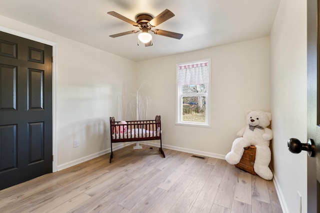 bedroom with ceiling fan, light hardwood / wood-style flooring, and a crib