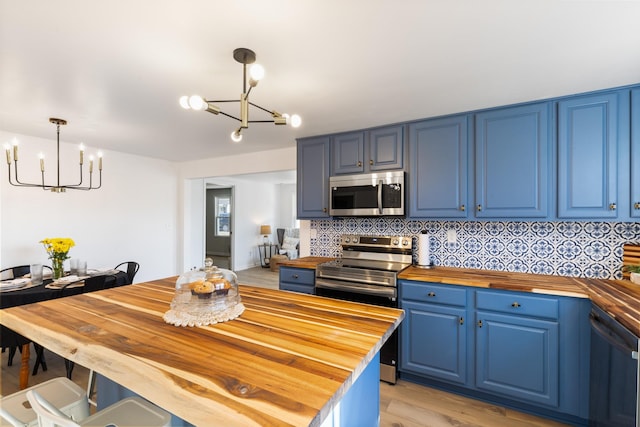 kitchen with pendant lighting, butcher block countertops, blue cabinetry, backsplash, and stainless steel appliances