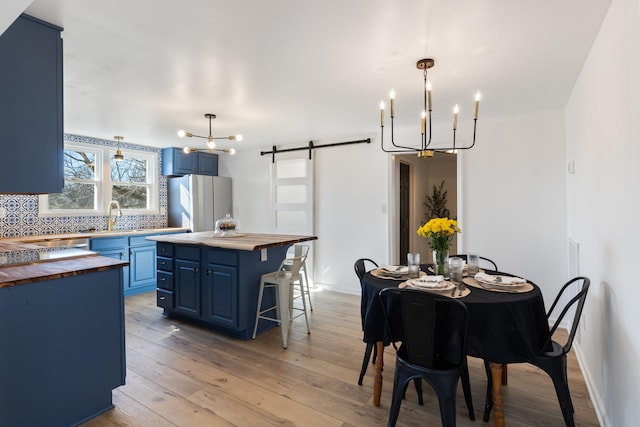 dining area featuring a barn door, sink, a chandelier, and light wood-type flooring