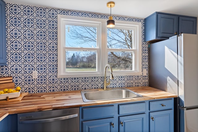 kitchen featuring decorative light fixtures, blue cabinets, sink, wooden counters, and stainless steel dishwasher