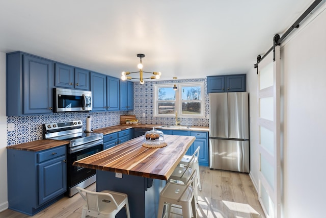 kitchen featuring blue cabinets, wooden counters, hanging light fixtures, stainless steel appliances, and light wood-type flooring