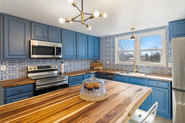 kitchen with sink, butcher block counters, stainless steel appliances, blue cabinets, and decorative light fixtures