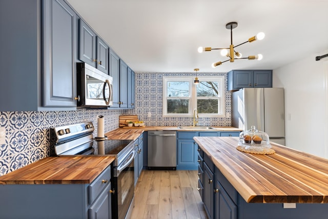 kitchen with appliances with stainless steel finishes, butcher block countertops, blue cabinets, sink, and hanging light fixtures