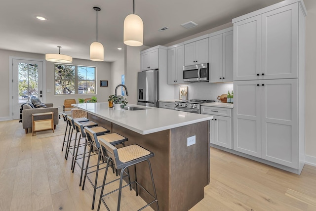 kitchen with sink, a breakfast bar, appliances with stainless steel finishes, hanging light fixtures, and a center island with sink