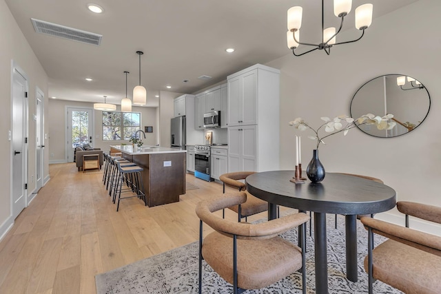 dining room with a notable chandelier, sink, and light wood-type flooring